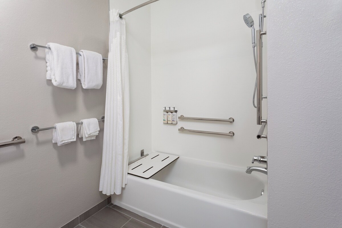A modern bathroom with a bathtub, shower, and handrails.