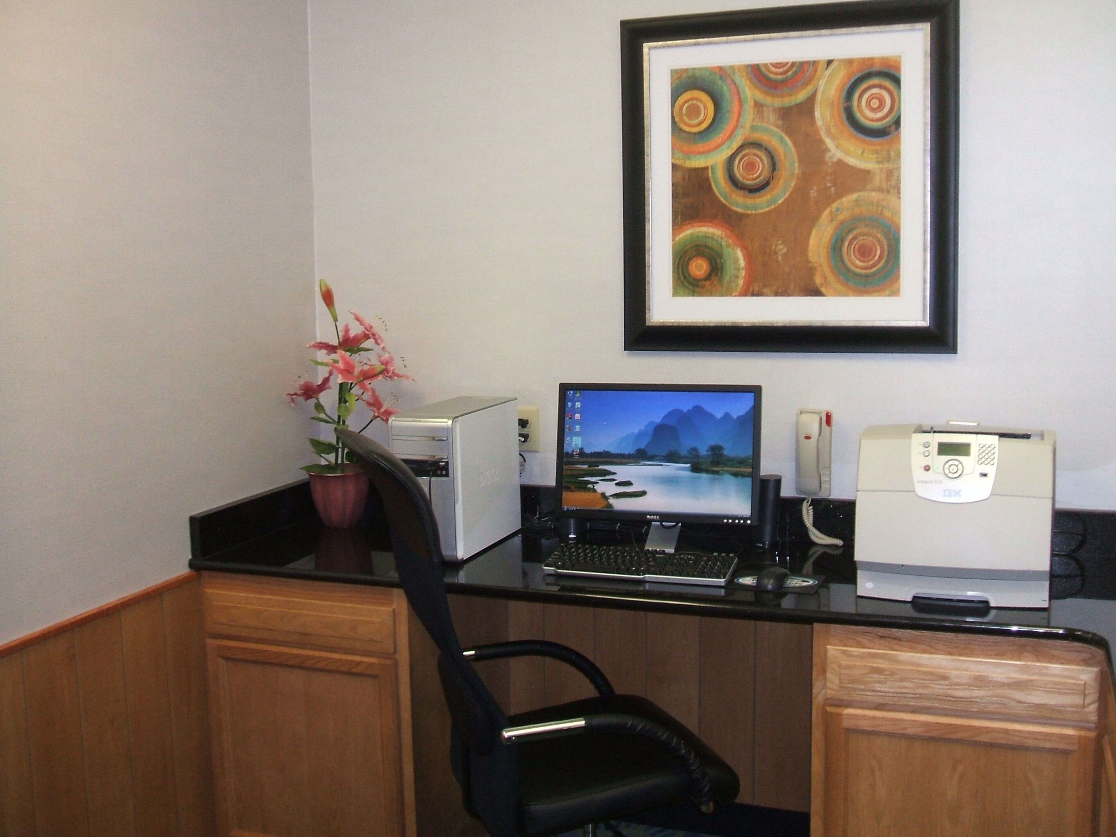Ein Home-Office-Arbeitsplatz mit einem Desktop-Computer, einem Bildschirm, einem Drucker und einem gerahmten abstrakten Gemälde an der Wand.