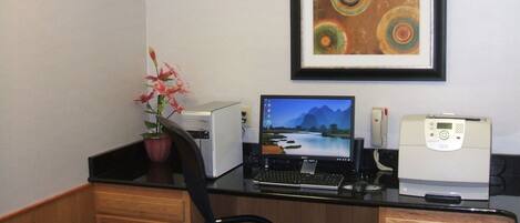 Ein Home-Office-Arbeitsplatz mit einem Desktop-Computer, einem Bildschirm, einem Drucker und einem gerahmten abstrakten Gemälde an der Wand.