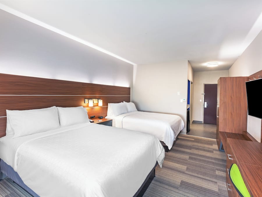 A hotel room with two beds, a flat-screen TV, and a desk with a lamp.