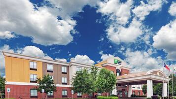 Een meerlaags hotel met een opvallende ingang, aangepaste parkeerplaatsen en een heldere lucht met wolken.
