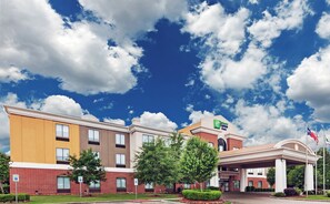Un hotel de varios pisos con una entrada destacada, estacionamiento accesible y un cielo despejado con nubes.