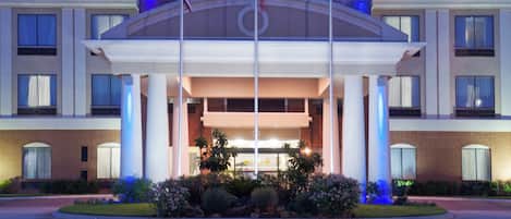 A Holiday Inn Express & Suites hotel with a prominent entrance, flagpoles, and a landscaped front garden.