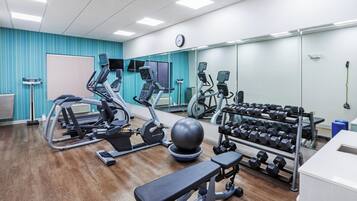 Un gimnasio con máquinas de cardio, pesas libres y un espejo grande.