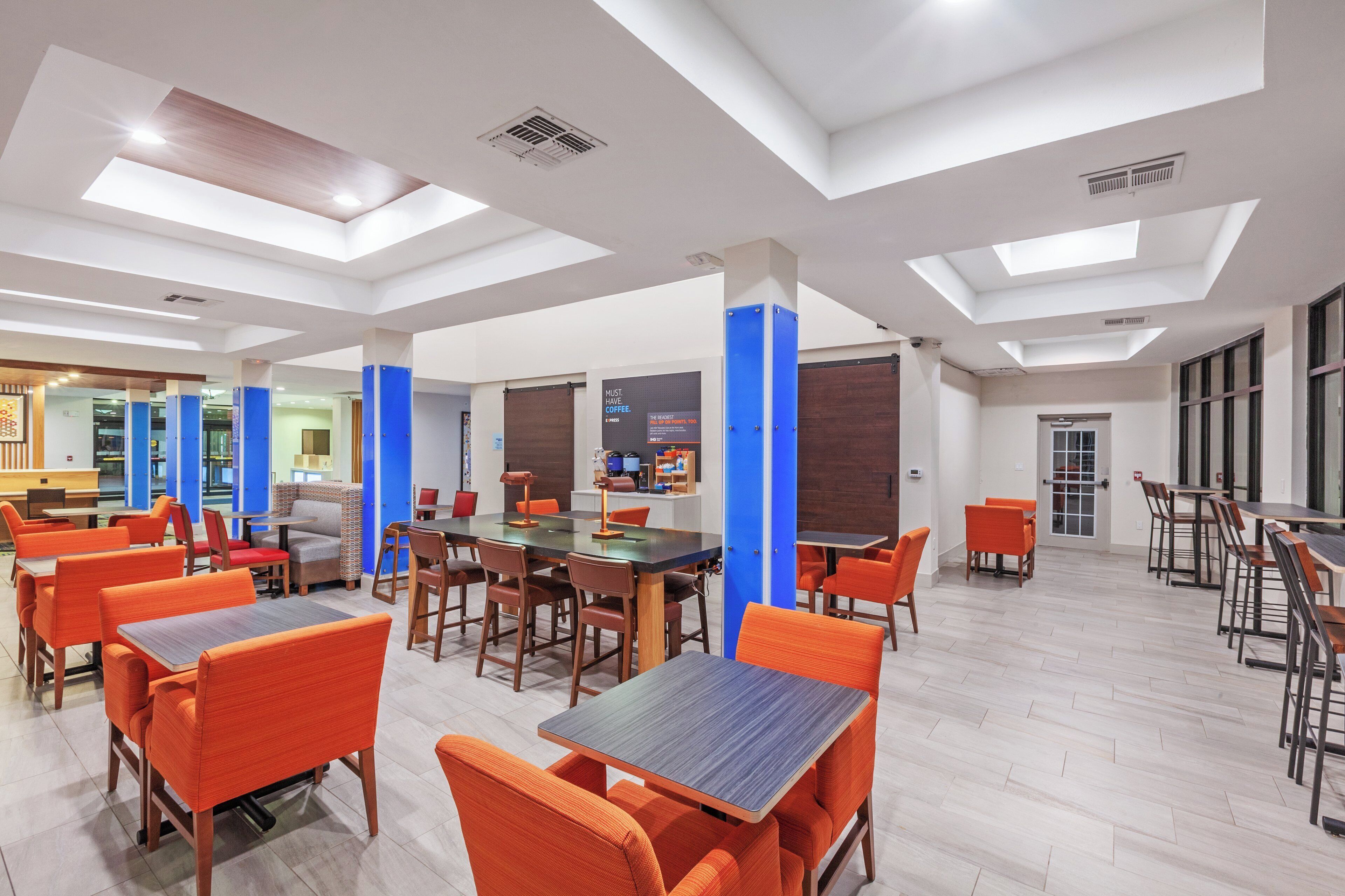 A modern dining area with multiple tables and chairs, a coffee station, and a view of the outside through large windows.