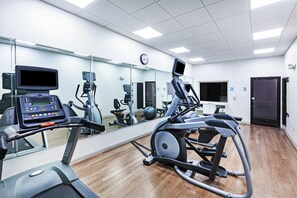 Une salle de sport équipée de matériel d’exercice, avec un grand miroir et une horloge au mur.