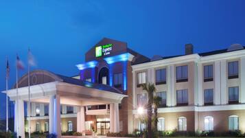 Un hotel Holiday Inn Express con entrada despejada, zona de estacionamiento techada y fachada bien iluminada.