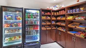 A food service area with a refrigerated display case and shelves stocked with snacks and beverages.