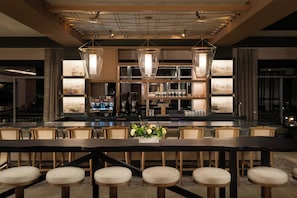 A bar area with a long counter, multiple seating options, and a coffee machine. - The Harborvale, Autograph Collection (Burlington)