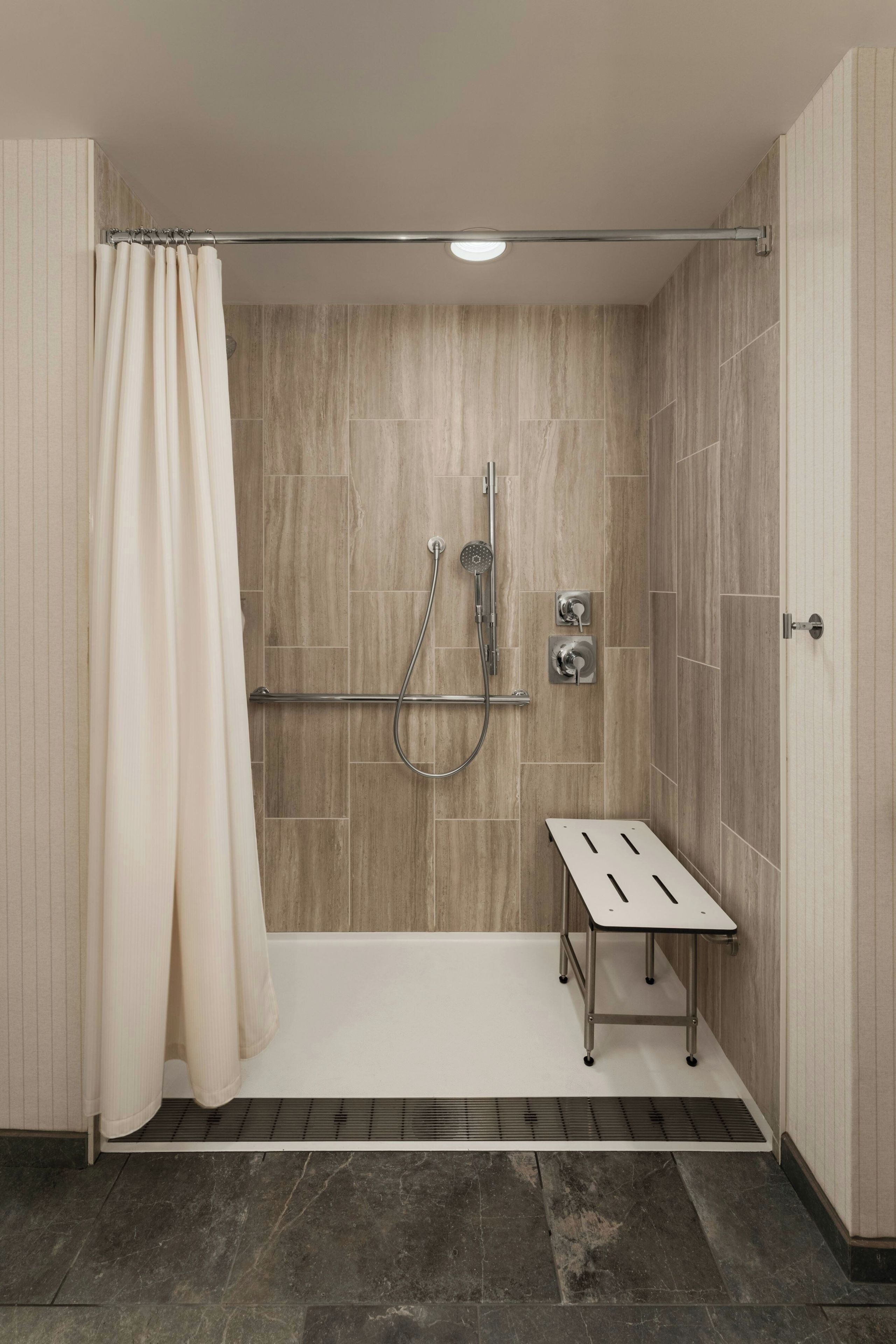 A modern shower area with a glass door, a handheld showerhead, a wall-mounted faucet, and a small bench.