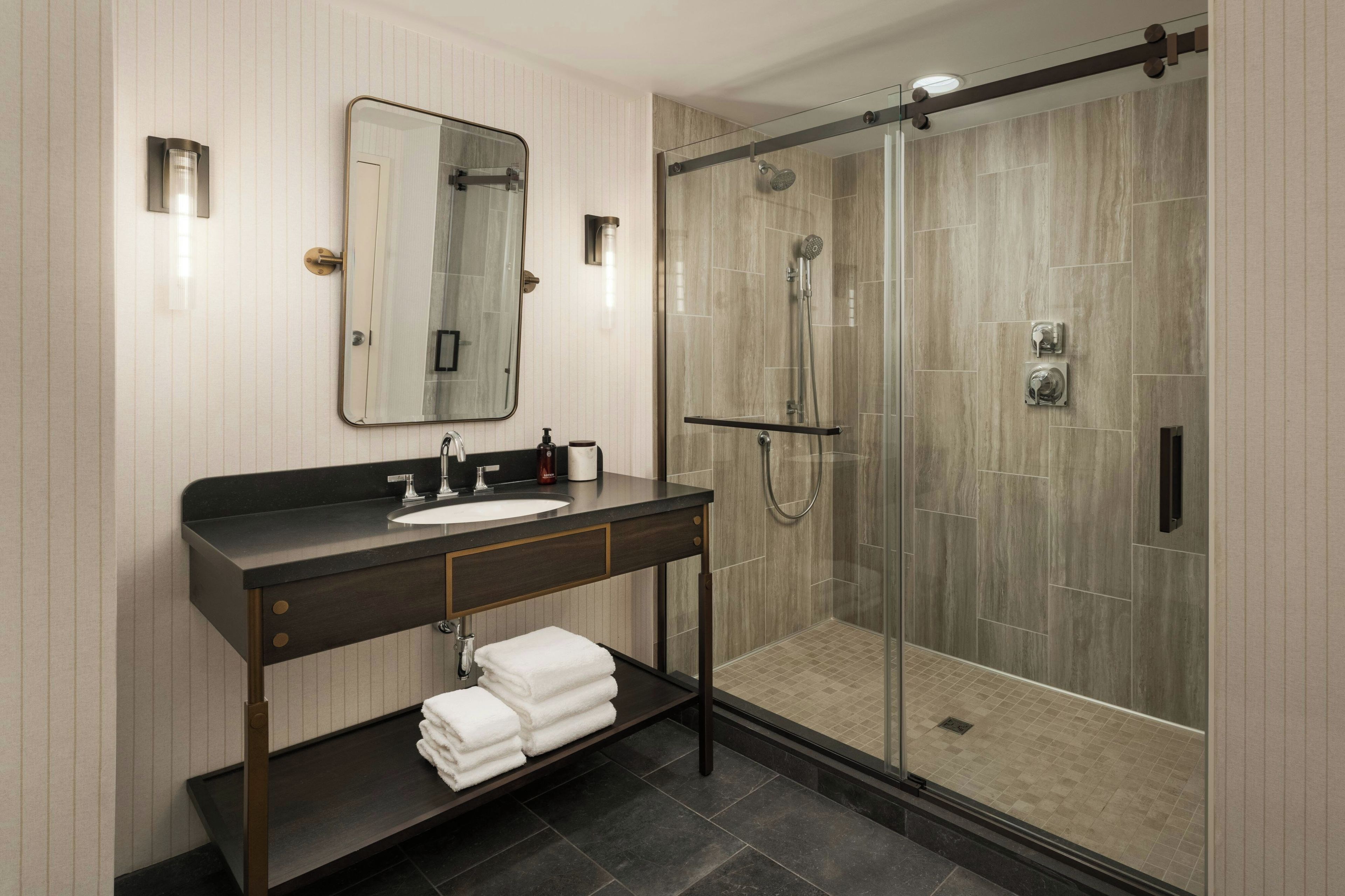 A modern bathroom with a glass-enclosed shower, a vanity with a sink, and a mirror.