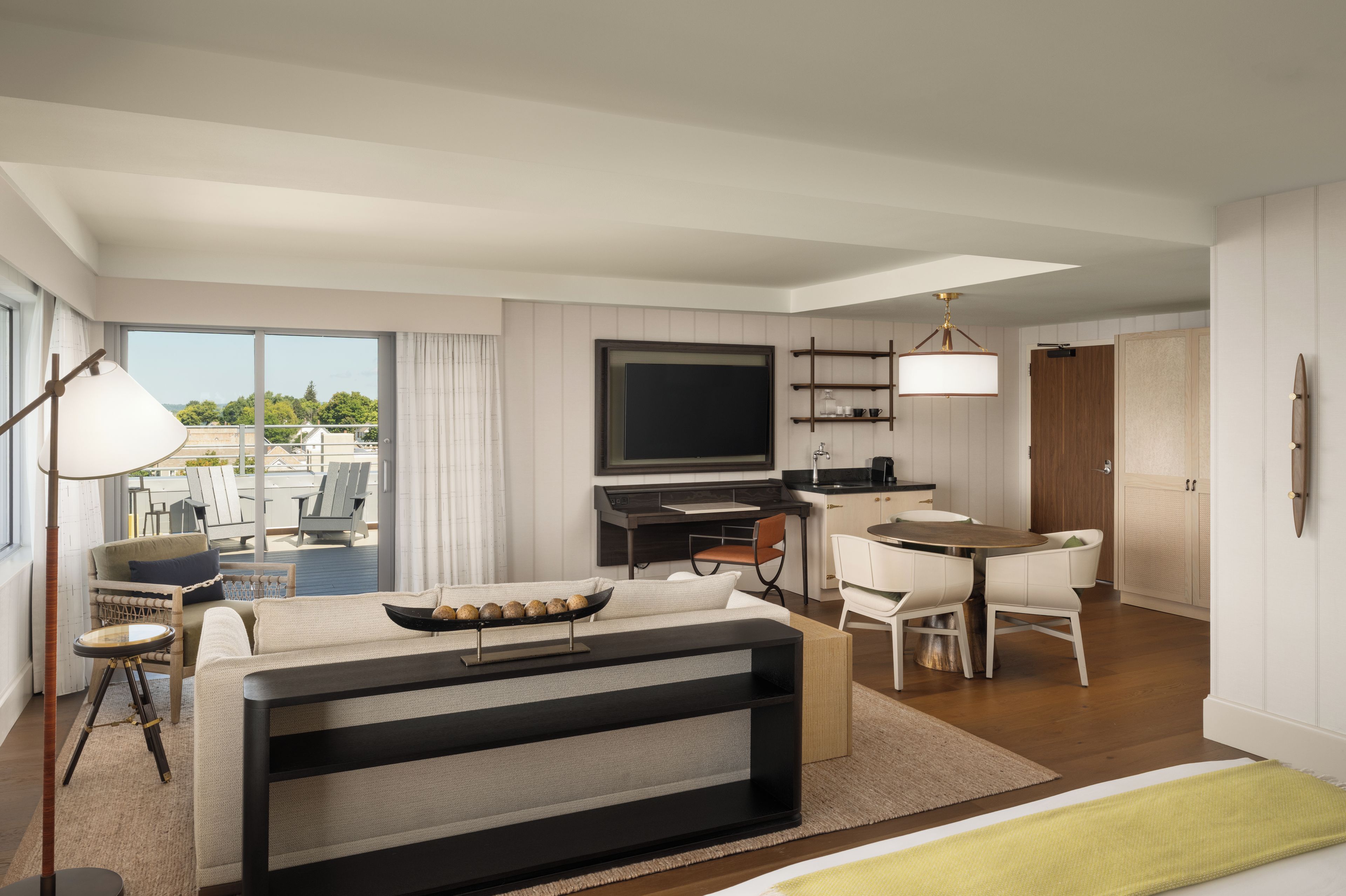A modern hotel room with a large bed, a desk, a television, and a balcony with outdoor seating.