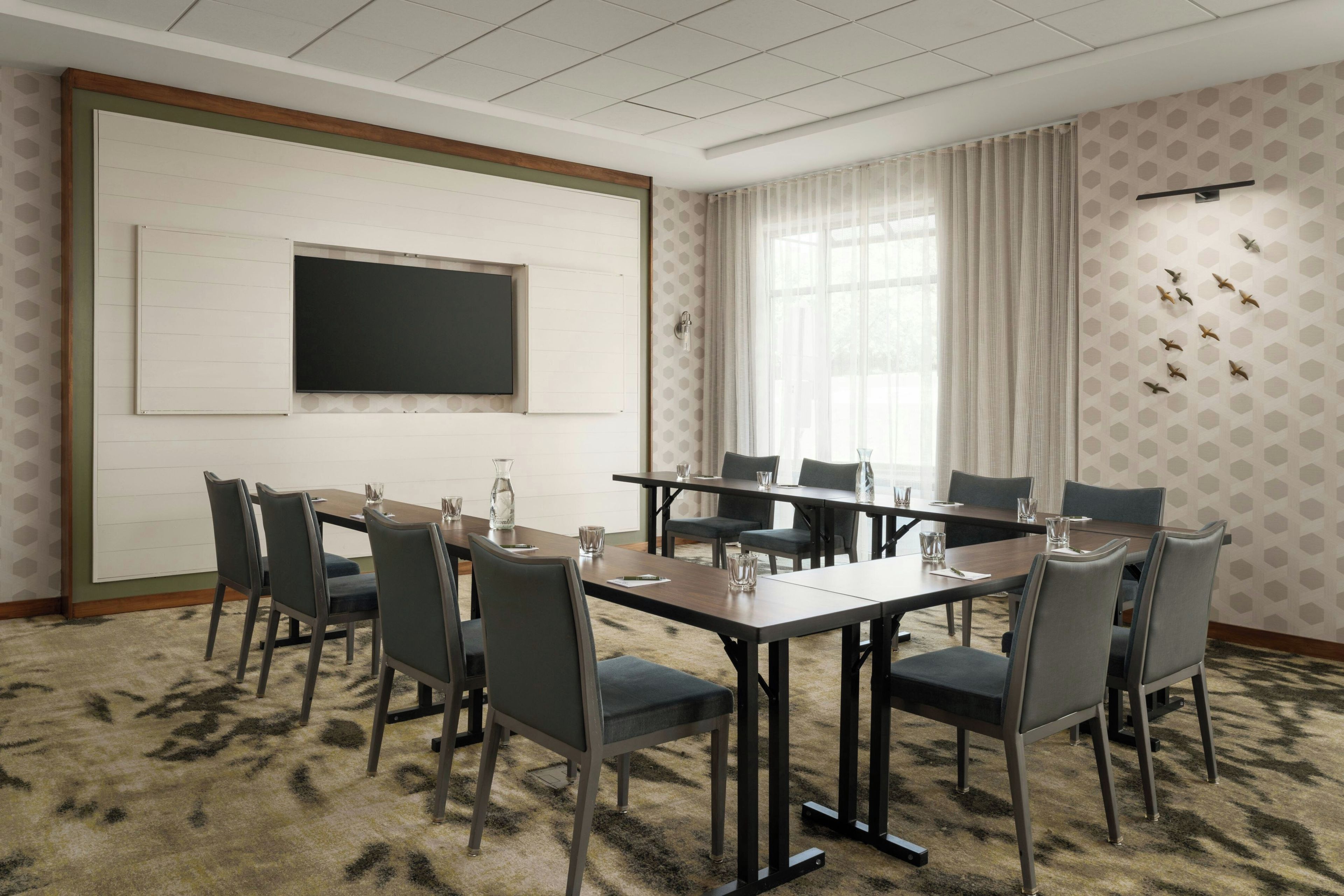 Ein Konferenzraum mit großem Tisch, Stühlen, einer Projektionsleinwand und einer Wand mit Muster.