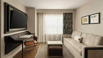 A modern hotel room with a flat-screen TV, a sofa, a desk, and a chair.