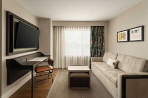 A modern hotel room with a flat-screen TV, a sofa, a desk, and a chair.