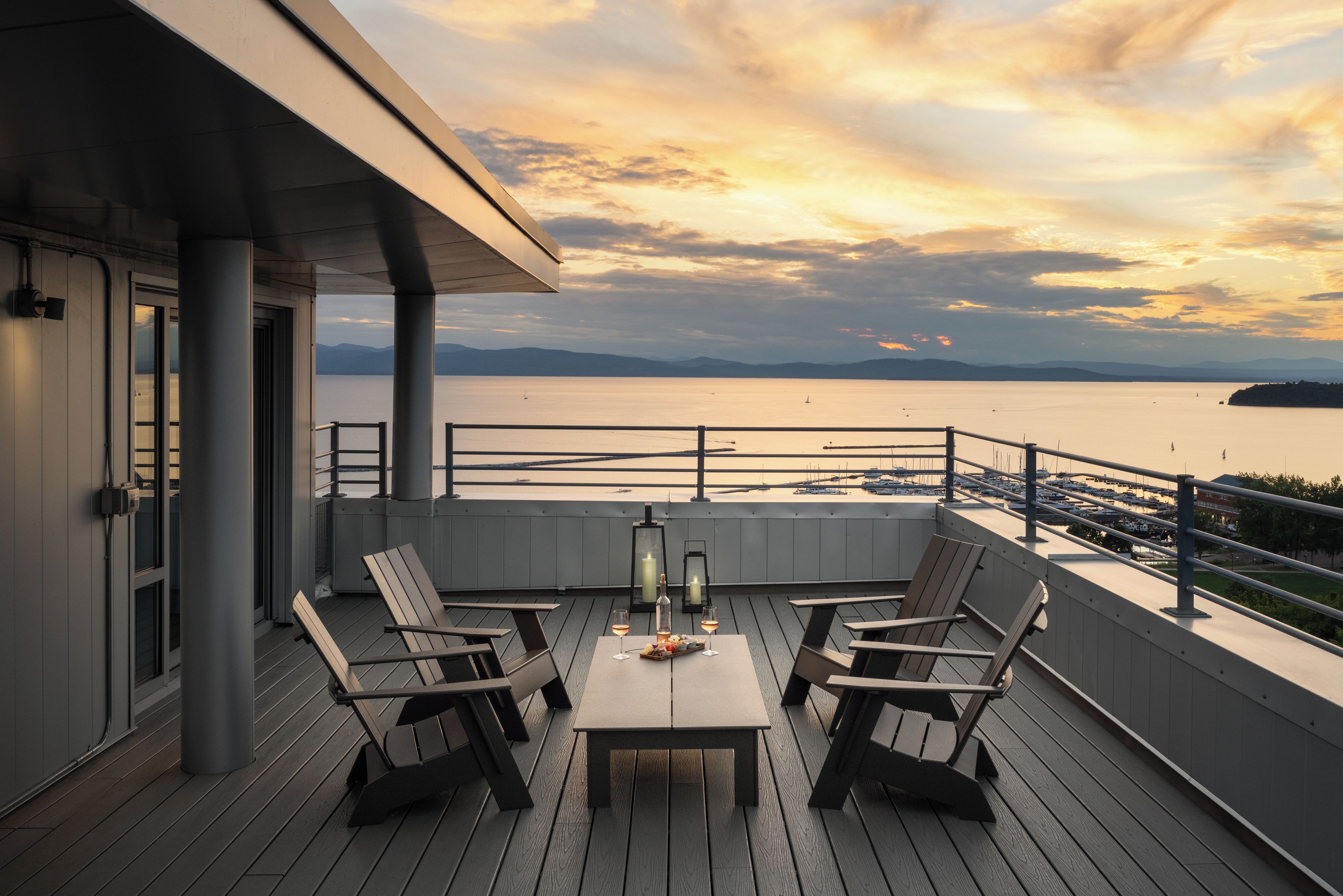 A deck with a table and chairs, overlooking a marina with boats and a calm sea.
