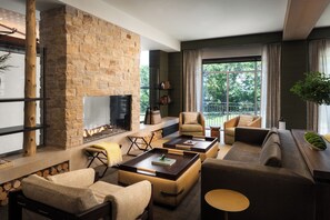 A modern living room with a stone fireplace, leather sofas, and a large window offering a view of the outdoors. - The Harborvale, Autograph Collection (Burlington)