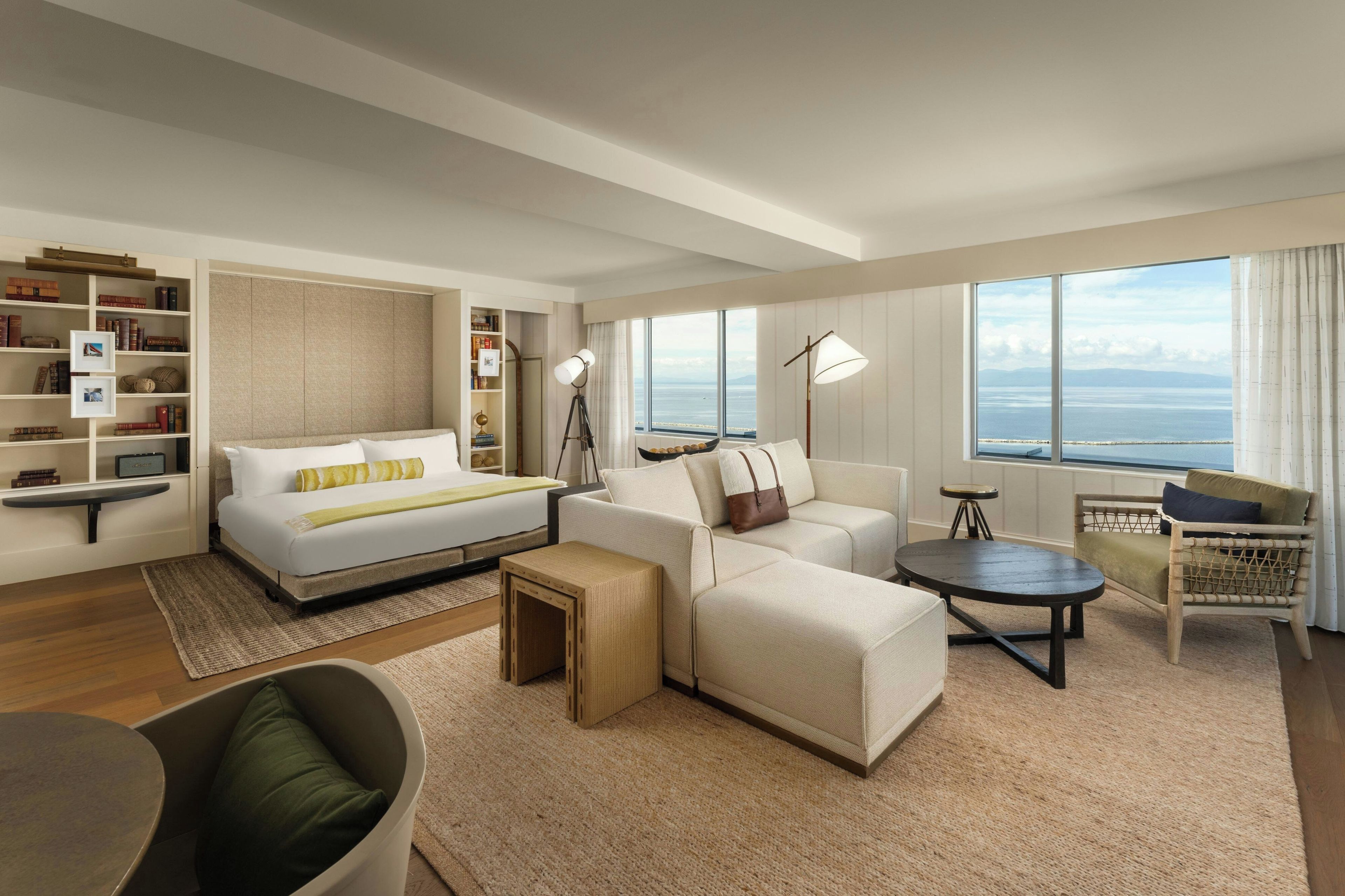 Una habitación de hotel moderna con cama, sofá, sillón y vista al mar.