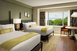 A hotel room with two beds, a desk, a chair, a window with a view, and a lamp.