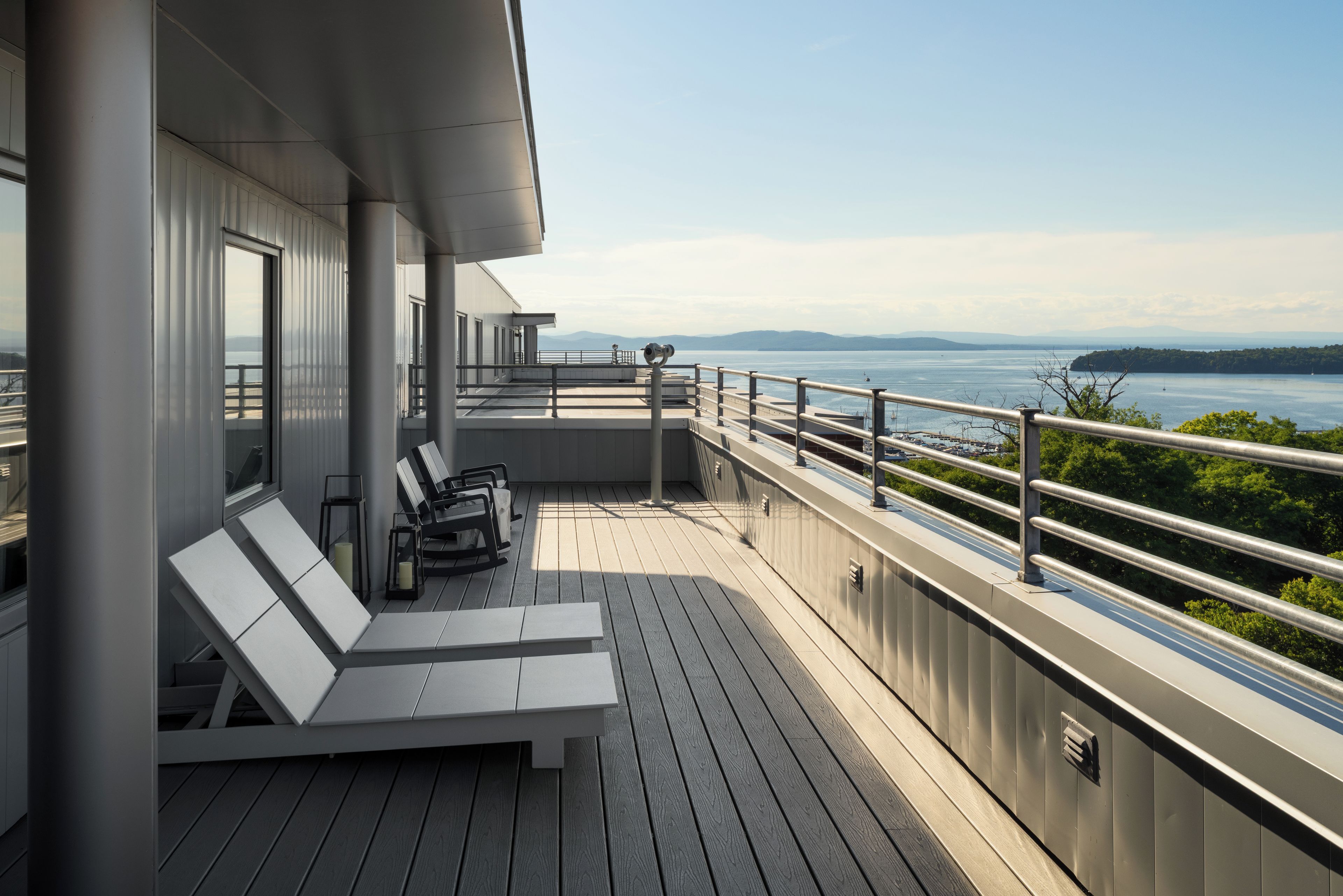 A deck with lounge chairs and a table, overlooking a body of water with distant land.