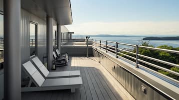 A deck with lounge chairs and a table, overlooking a body of water with distant land.