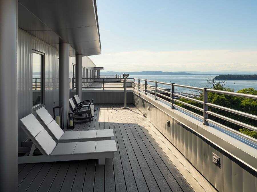 Terraza con sillones y una mesa, con vista a un cuerpo de agua y tierra a lo lejos.