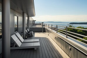 A deck with lounge chairs and a table, overlooking a body of water with distant land.