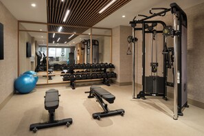 A gym with exercise equipment, a bench, and a mirrored wall. - The Harborvale, Autograph Collection (Burlington)