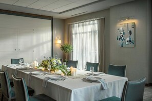 A conference room with a long table set for a meeting, equipped with chairs, a plant, candles, and a painting on the wall.