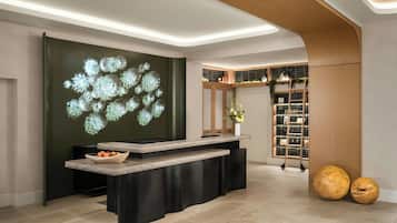 A reception area with a modern design, including a curved reception desk, a wall-mounted light display, and a shelving unit with various items.