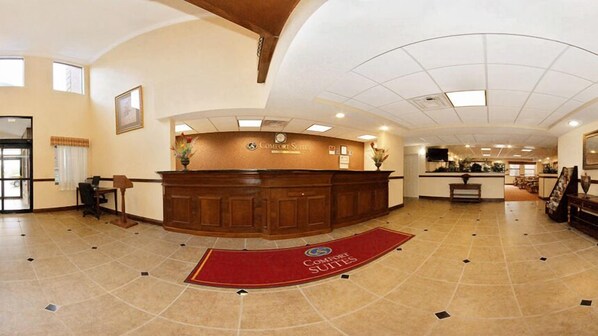 A hotel reception area with a curved wooden reception desk, a red carpet, and a tiled floor.