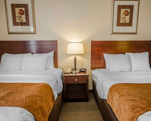 A hotel room with two beds, a nightstand with a lamp, a telephone, and framed floral artwork on the walls.