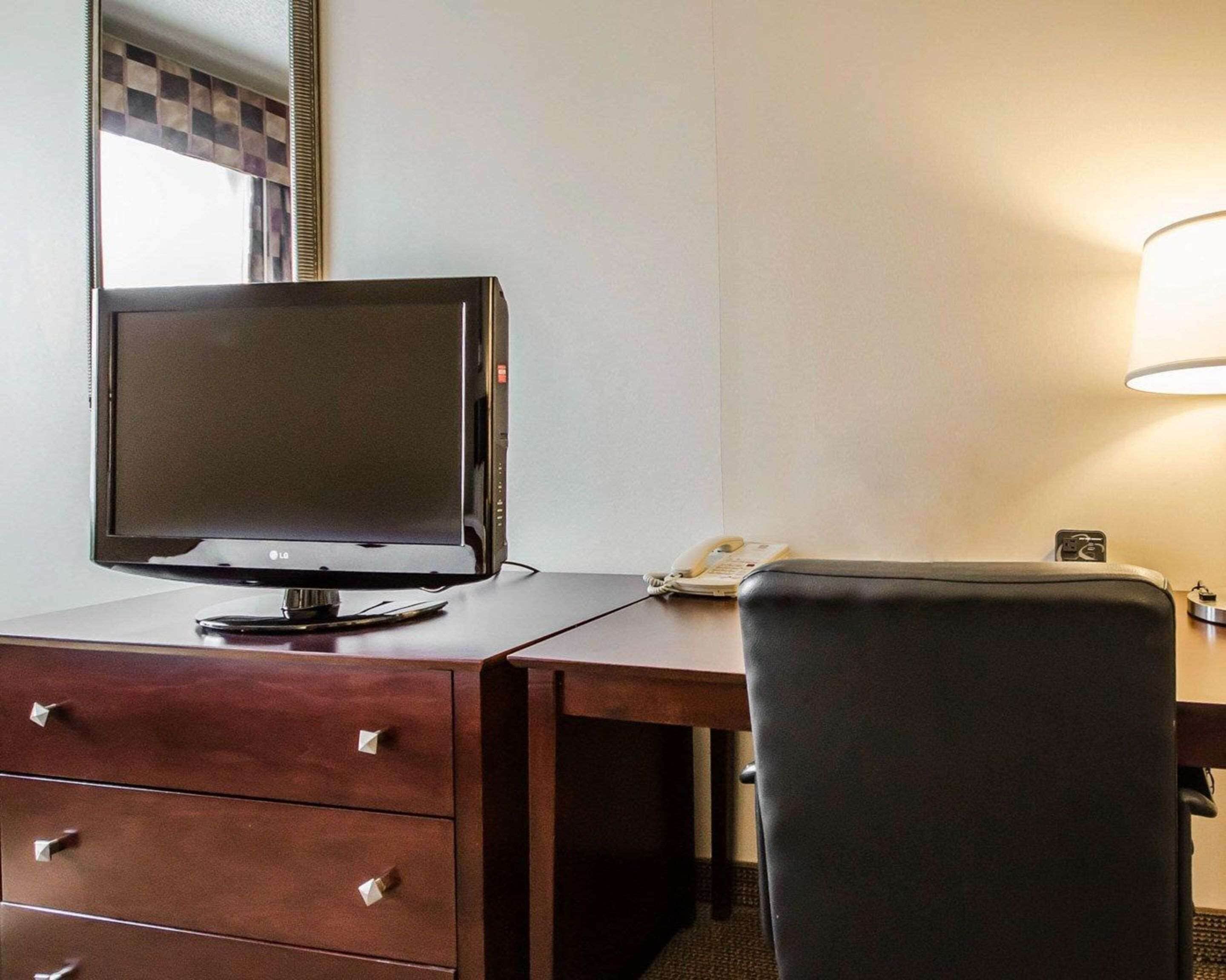 Una camera d'albergo con una scrivania, una TV a schermo piatto, un telefono e una sedia.