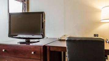 Una camera d'albergo con una scrivania, una TV a schermo piatto, un telefono e una sedia.