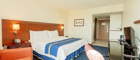 A hotel room with a large bed, a desk with a computer, a chair, a phone, and a TV.