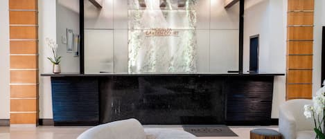 A reception desk with a marble top, a wooden panel wall, and a reception area with a sofa and a small round table.
