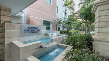 A hotel with a garden court, a pool with a waterfall, and lush greenery.