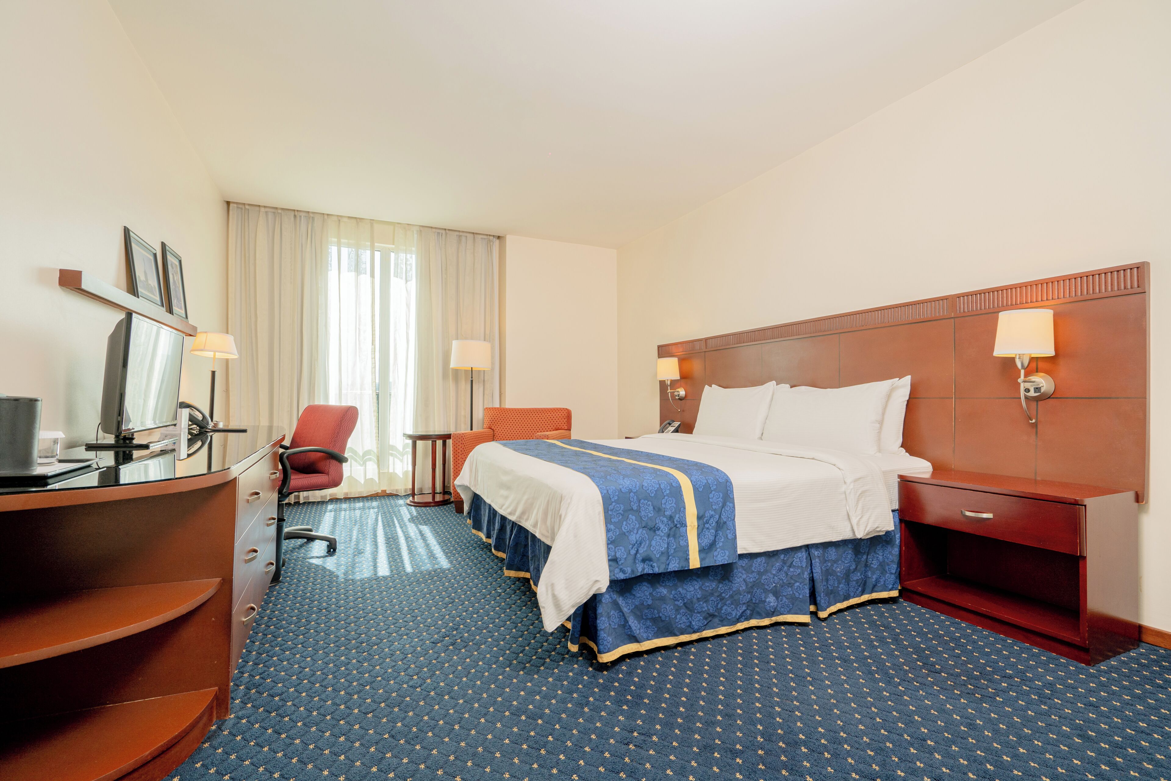 A hotel room with a bed, desk, chair, and a view of the outdoors.