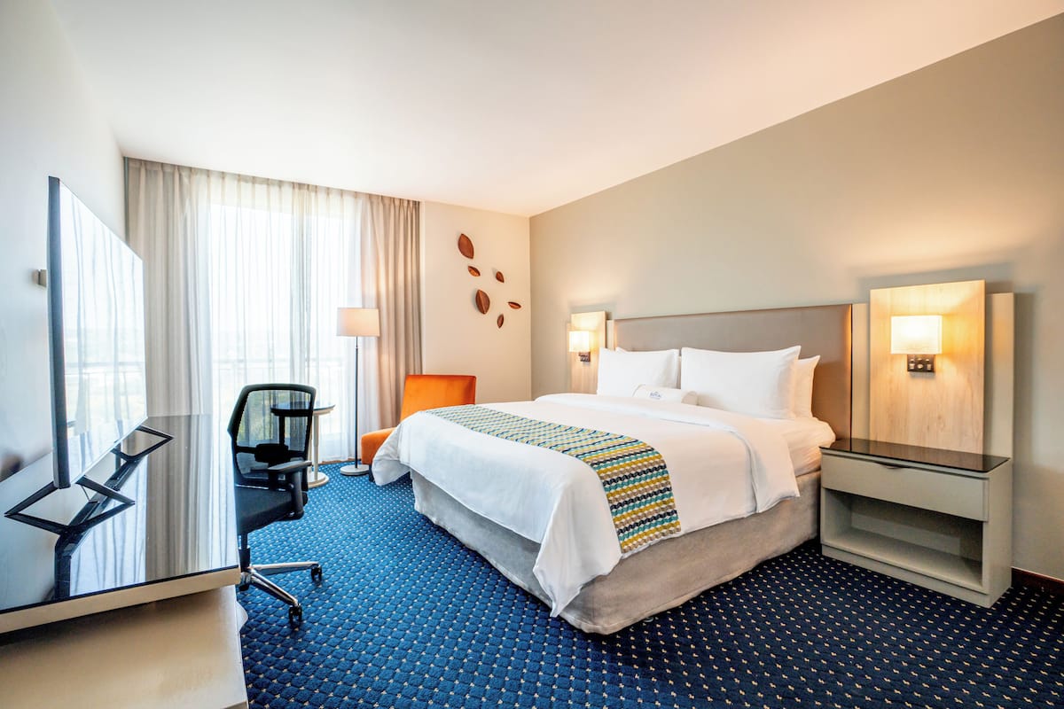 Quarto de hotel com cama, escrivaninha, cadeira, mesa de cabeceira e espelho.