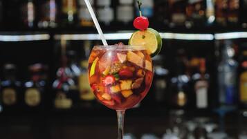 Een cocktail met fruitdecoratie en een kers op een glazen steel, geplaatst op een bar achtergrond met flessen.