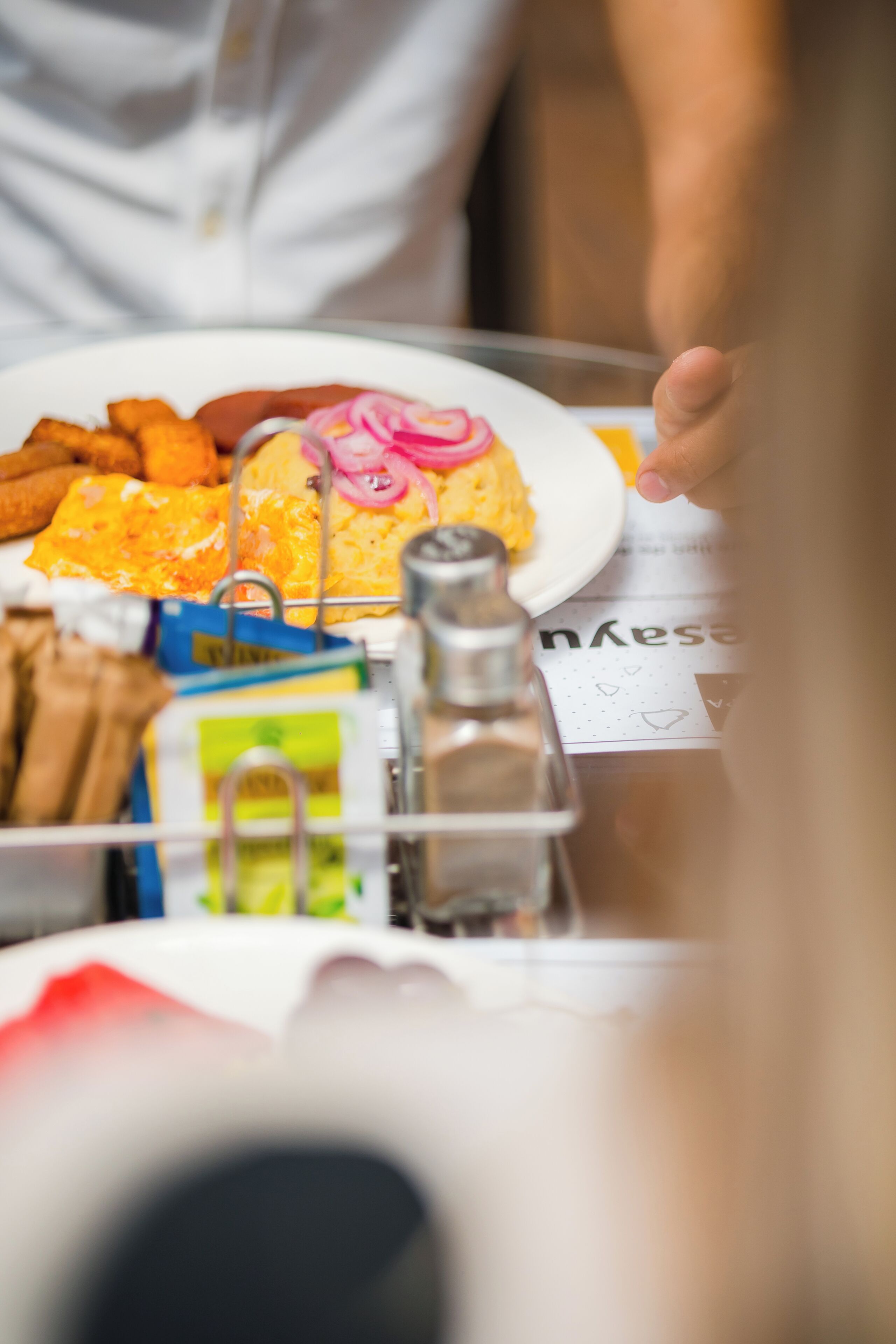 A table with a plate of food, including eggs and fries, and a salt shaker.