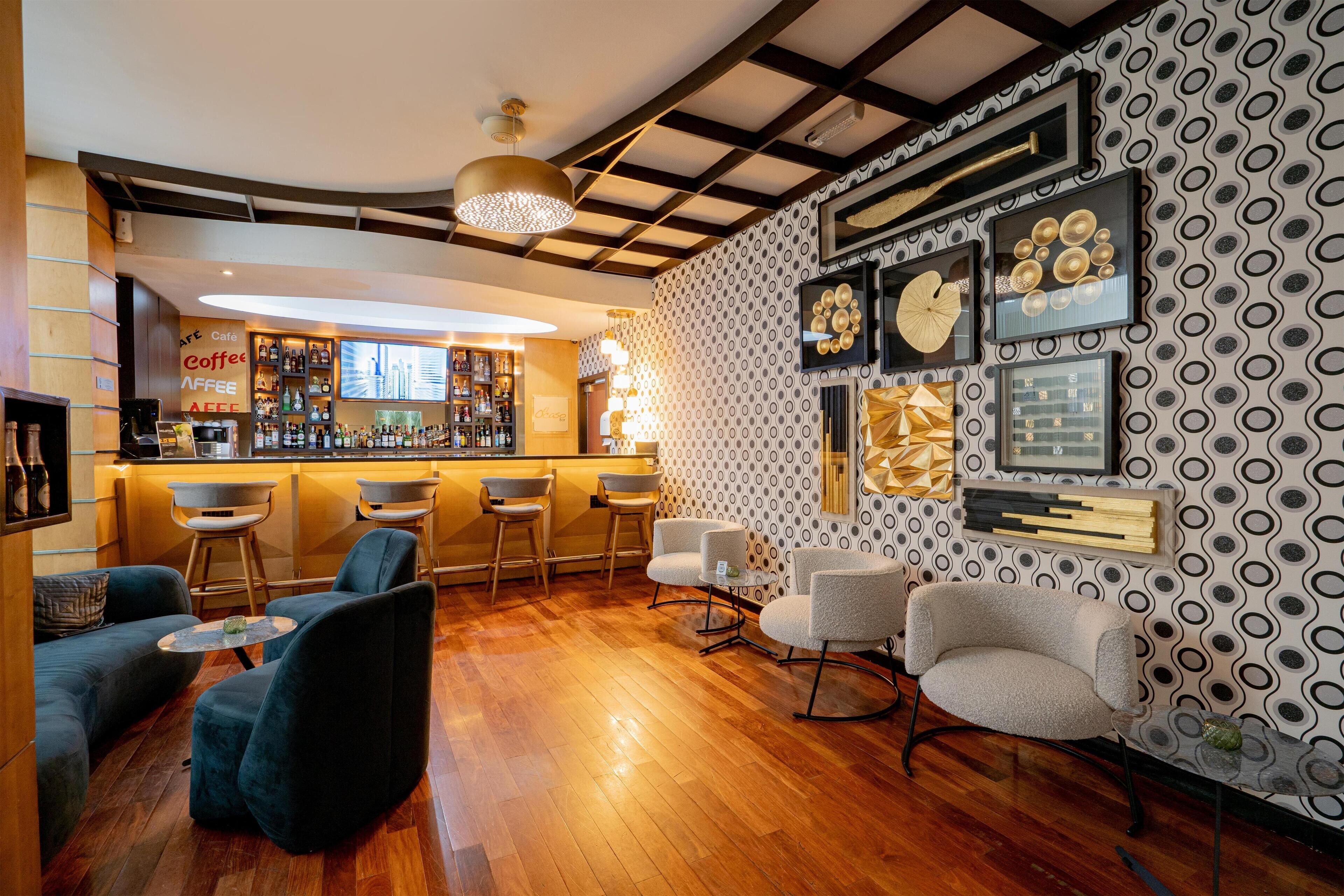 A bar area with stools, a counter, and a wall with framed pictures and a patterned wallpaper.