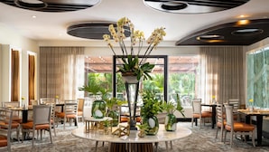 A modern dining area with round tables, chairs, and potted plants. - Hodelpa Garden Court (Punal)