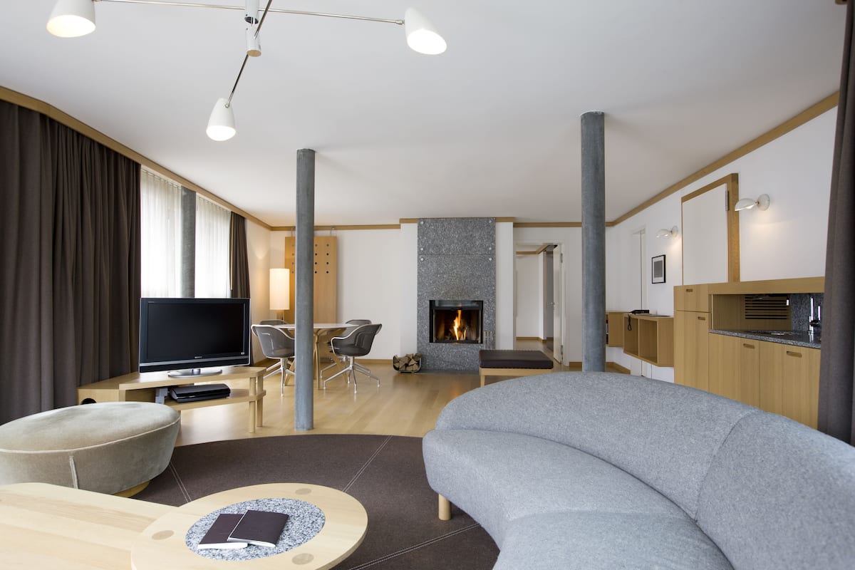 Una sala de estar moderna con un televisor de pantalla plana, un sofá gris, una mesa de centro redonda y una chimenea.