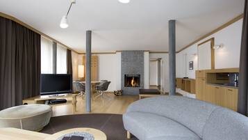 Een moderne woonkamer met een flatscreen televisie, een grijze bank, een ronde salontafel en een open haard.