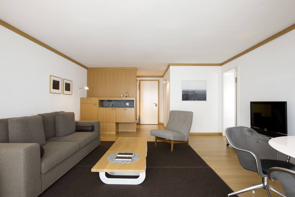 Una sala de estar moderna con un sofá, una mesa de centro, un televisor y una cocina al fondo.