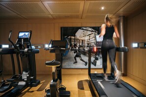 A gym with treadmills, stationary bikes, and a large screen displaying a runner.