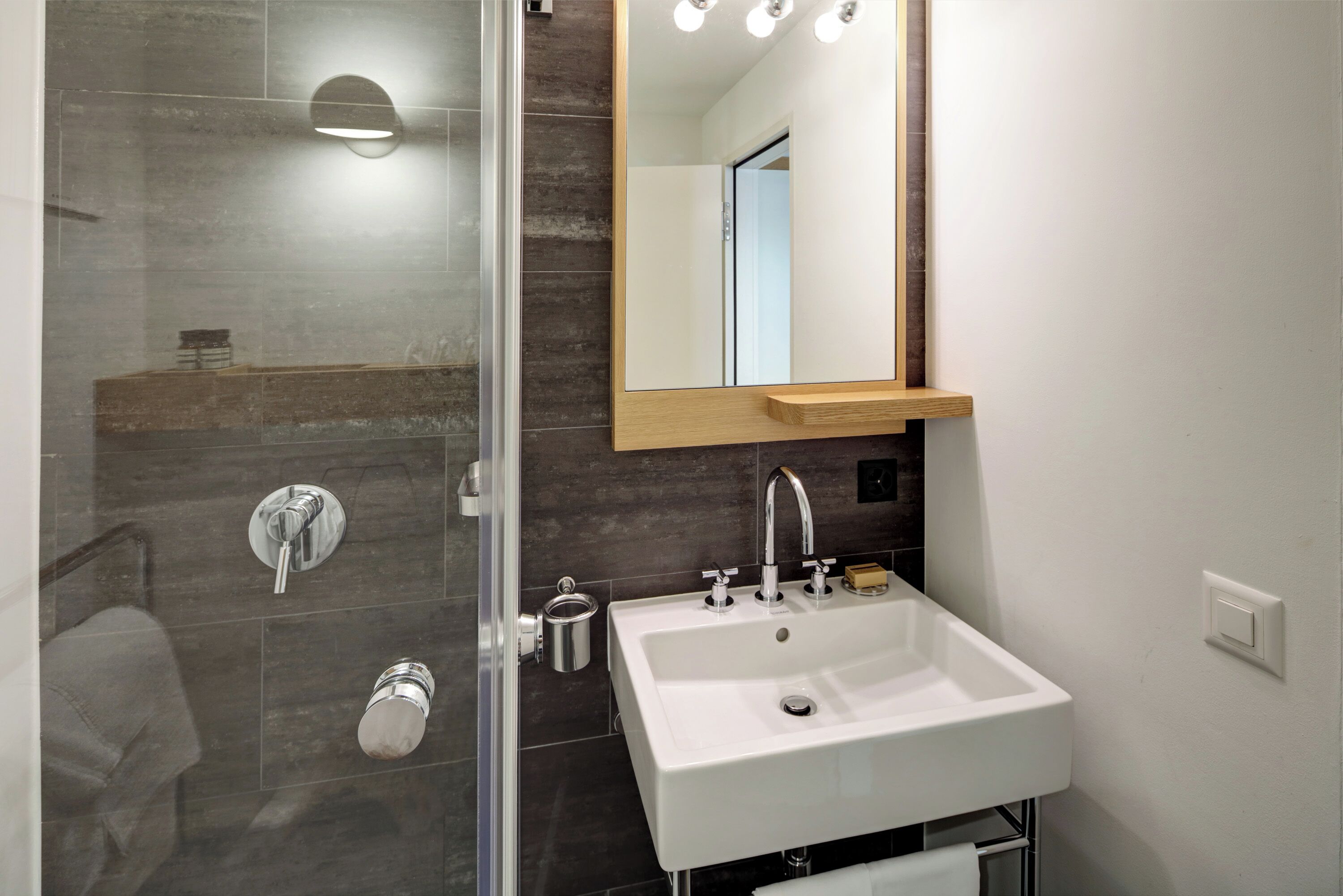 Een moderne badkamer met een douchecabine van glas, een witte wastafel en een spiegel met ingebouwde verlichting.