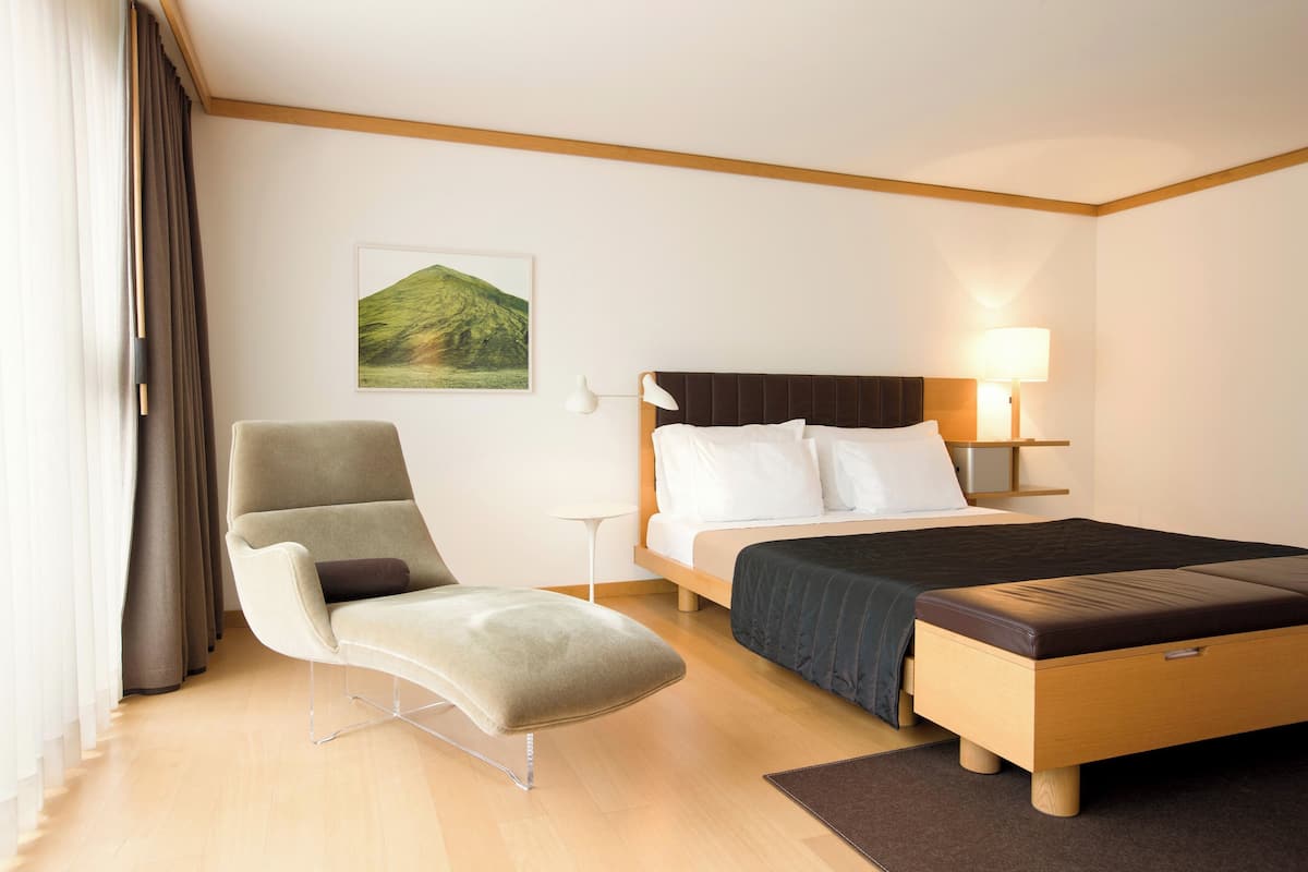 Una habitación de hotel con una cama, una silla, una mesita de noche y una lámpara.