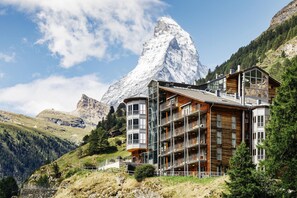 A multi-story building with balconies, set against a mountainous backdrop. - THE OMNIA - Design Mountain Lodge and Spa with Iconic Matterhorn Views (Zermatt)